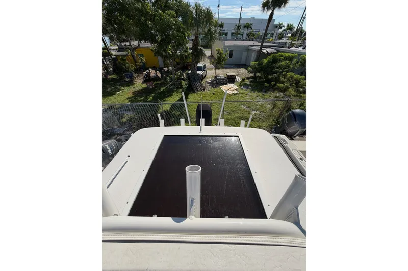 Slide: The Image of 2021 Caymas 28 HB boat deck with rod holders, surrounded by greenery and buildings. - 9