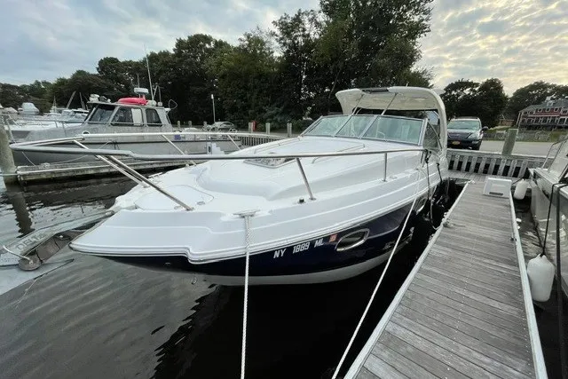 Slide: The Image of 2015 Chaparral 310 Signature boat docked at marina, surrounded by trees and other boats. - 4