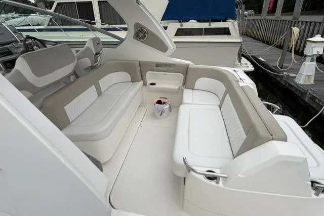 Slide: The Image of 2015 Chaparral 310 Signature boat interior with white and beige seating at a dock. - 11