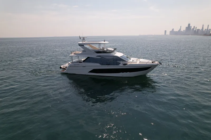 Slide: The Image of The 2022 Absolute 62 Fly cruises on calm waters with a city skyline in the background. - 2