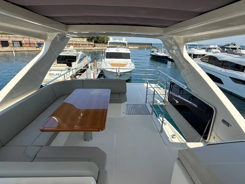 Slide: The Image of The image shows the deck of a 2022 Absolute 62 Fly, featuring a wooden table and seating. Several boats are visible in the harbor background. - 23