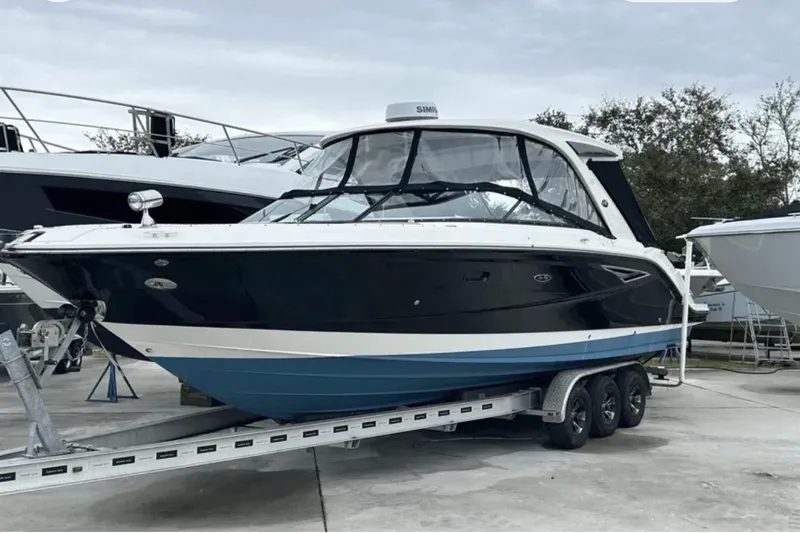 The Image of 2024 Sea Ray SLX 310 boat on trailer, sleek design, black and blue hull. - 13