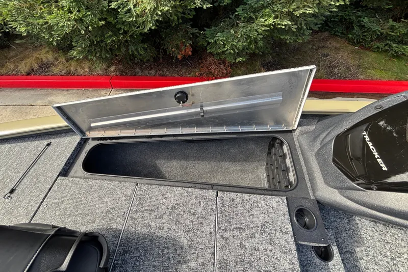 Slide: The Image of Open storage compartment on 2026 Tracker Pro Team 195 boat, surrounded by greenery. - 19
