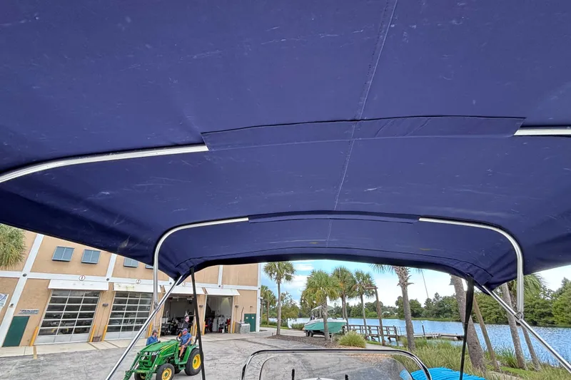 Slide: The Image of 2006 Sea Hunt Triton 186 boat with blue canopy, near a waterfront and building. - 13