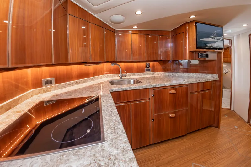 Slide: The Image of The yacht's kitchen features wooden cabinets, a stove, and a sink. A TV is mounted on the wall. - 26