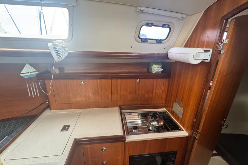 Slide: The Image of Compact kitchen area in a 2006 Hunter 31 sailboat with stove, fan, and wooden cabinetry. - 27