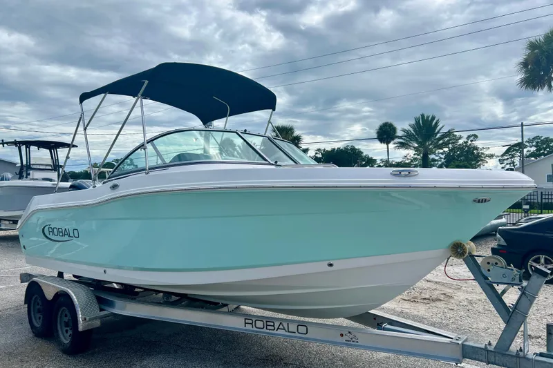 Slide: The Image of 2024 Robalo R207 Dual Console boat on trailer with canopy, parked outdoors. - 2