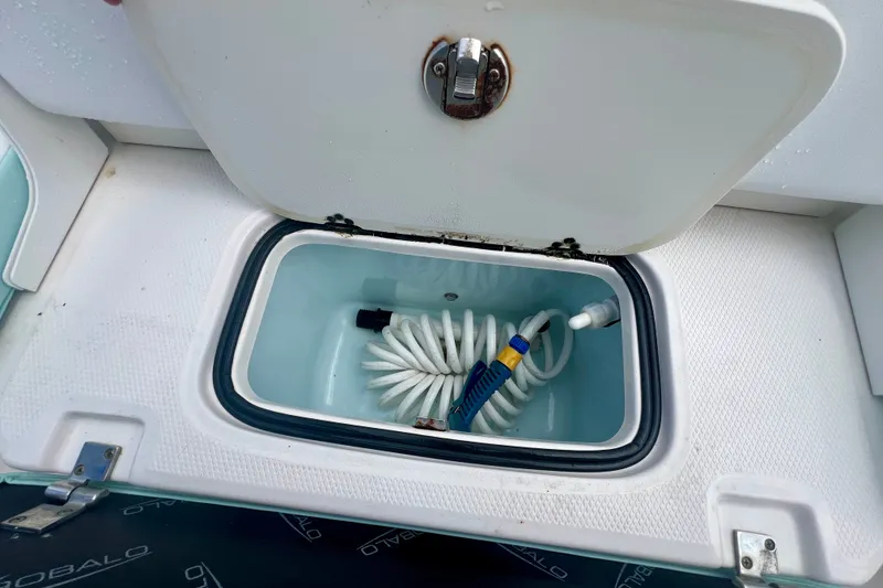 Slide: The Image of 2024 Robalo R207 Dual Console storage compartment with coiled hose and nozzle. - 10