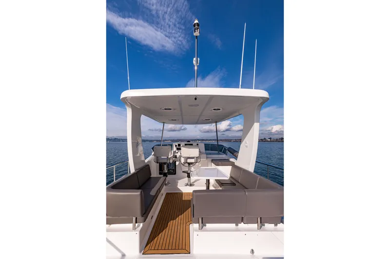 Slide: The Image of 2024 North Pacific 450 Pilothouse yacht deck with seating and helm, under clear blue sky. - 20