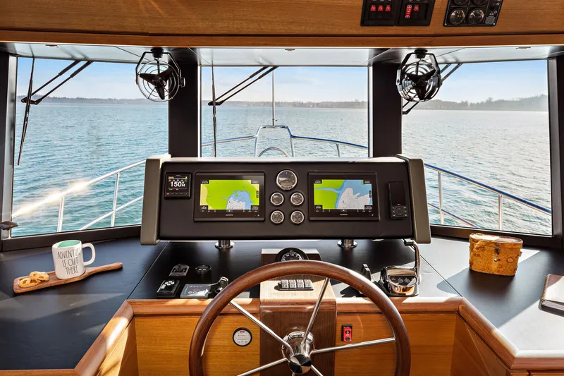 Slide: The Image of 2024 North Pacific 450 Pilothouse helm with navigation screens, steering wheel, and scenic ocean view. - 11