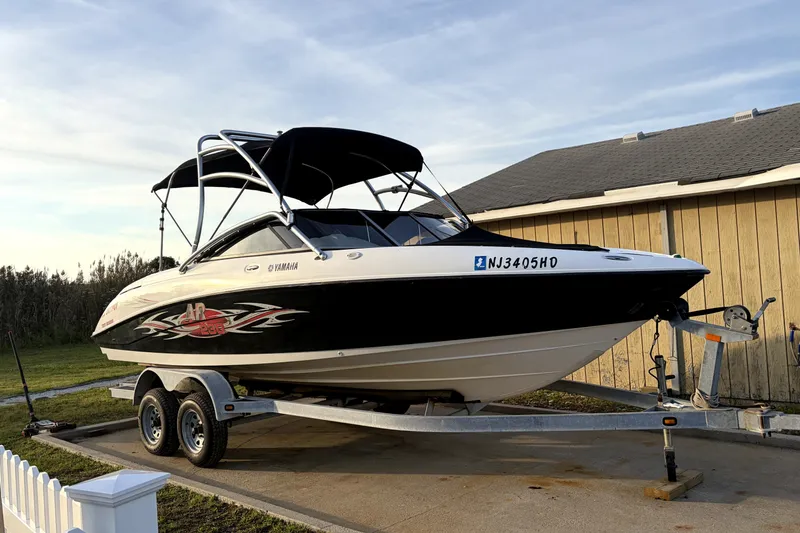 The Image of 2006 Yamaha Boats AR230 on trailer, parked beside a wooden building. - 0