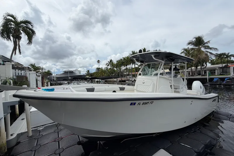 The Image of 2019 Mako 284 Center Console boat docked, surrounded by palm trees and cloudy sky. - 0