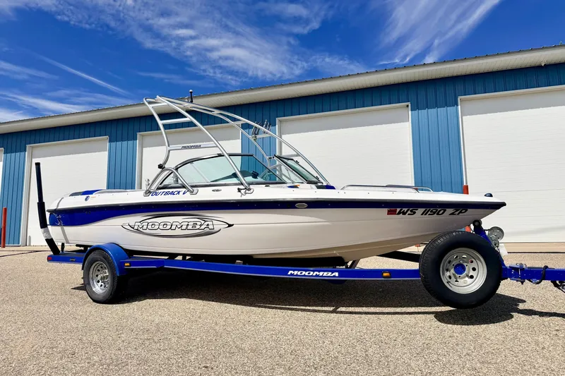 Slide: The Image of 2007 Moomba Outback V boat on trailer, parked outside blue building under clear sky. - 4
