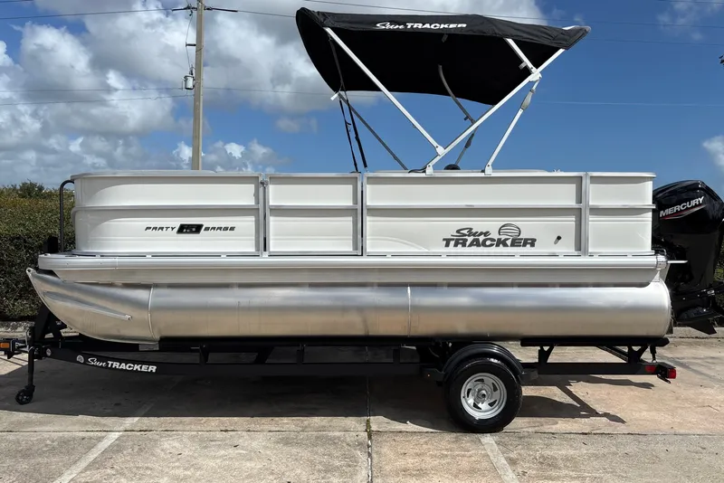 The Image of 2027 Sun Tracker Party Barge 18 DLX with a Bimini top on a trailer. - 0