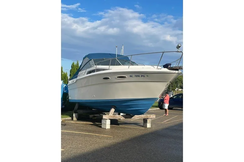 Slide: The Image of 1989 Sea Ray 300 Weekender boat on stands, blue hull, parked outdoors under a cloudy sky. - 37