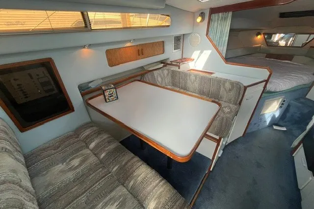Slide: The Image of 1989 Sea Ray 300 Weekender interior with dining area, cushioned seating, and cozy sleeping quarters. - 21