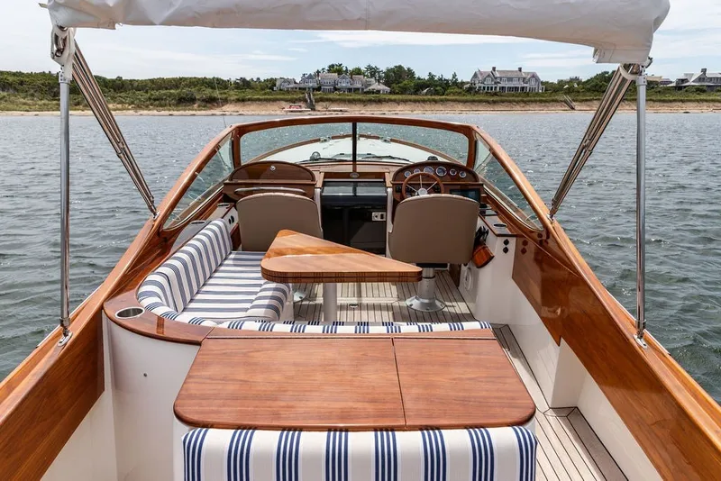Slide: The Image of 2025 Hinckley Yachts Talaria 29 Runabout with elegant wood finish and striped seating on water. - 15