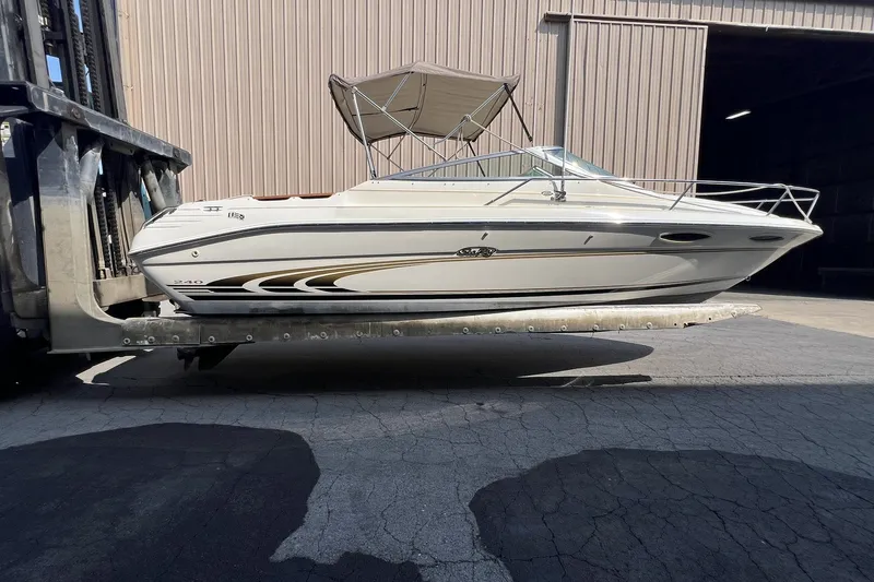 Slide: The Image of 1997 Sea Ray 240 Overnighter boat on forklift, beige exterior, parked outside warehouse. - 70