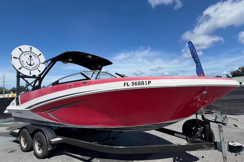 The Image of 2016 Glastron GT 245 boat in red on trailer, displayed outdoors under clear sky. - 0