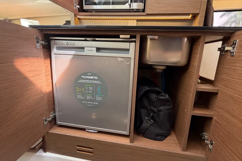Slide: The Image of Interior of 2021 Jeanneau Cap Camarat 9.0 WA showing compact kitchen with fridge and sink. - 12
