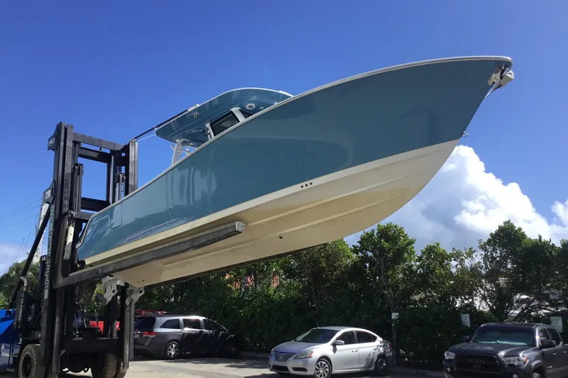 Slide: The Image of 2025 Sportsman Open 322 Center Console boat lifted by forklift under clear blue sky. - 75
