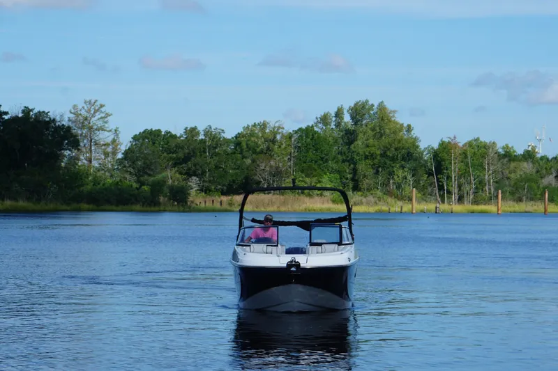 Slide: The Image of 2024 Hurricane SunDeck 2600 OB cruising on a serene lake with lush greenery. - 3