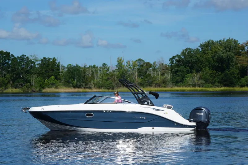 Slide: The Image of 2024 Hurricane SunDeck 2600 OB boat cruising on a serene lake with lush greenery. - 2
