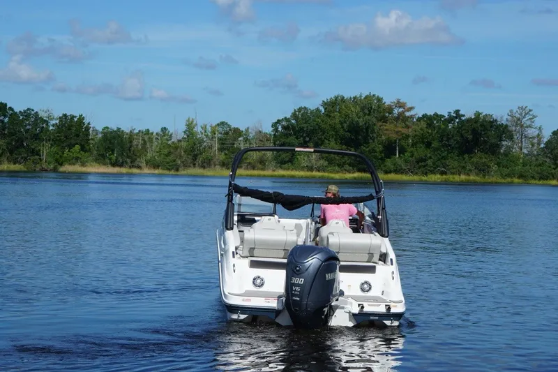 Slide: The Image of 2024 Hurricane SunDeck 2600 OB boat cruising on a serene lake with lush greenery. - 4