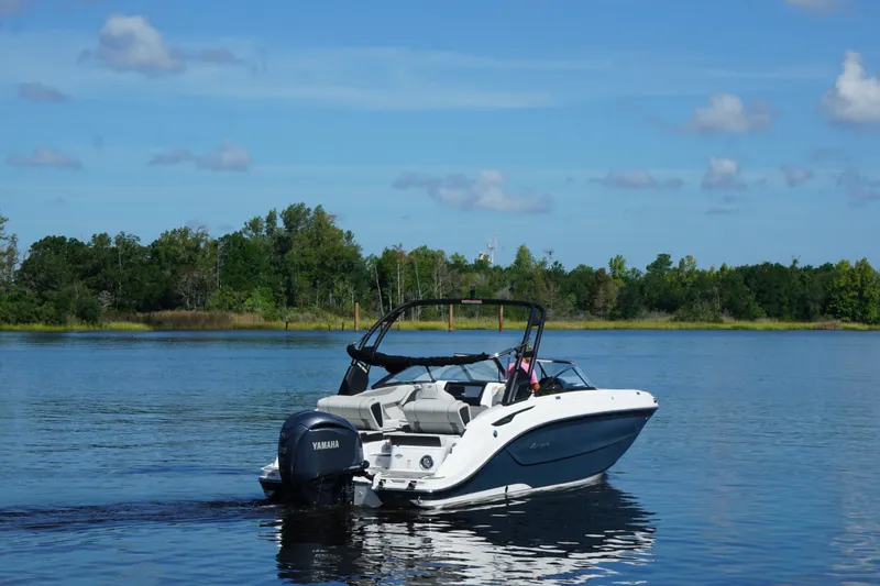 Slide: The Image of 2024 Hurricane SunDeck 2600 OB boat on a serene lake with lush green shoreline. - 1