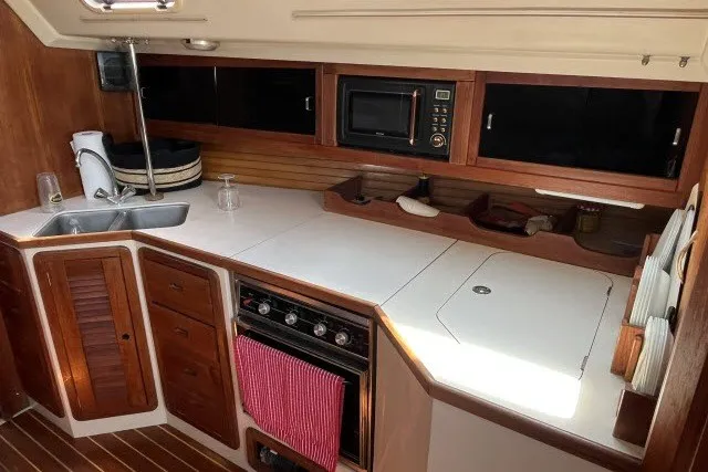 Slide: The Image of 1990 Catalina 42 yacht kitchen with sink, stove, microwave, and wooden cabinetry. - 4