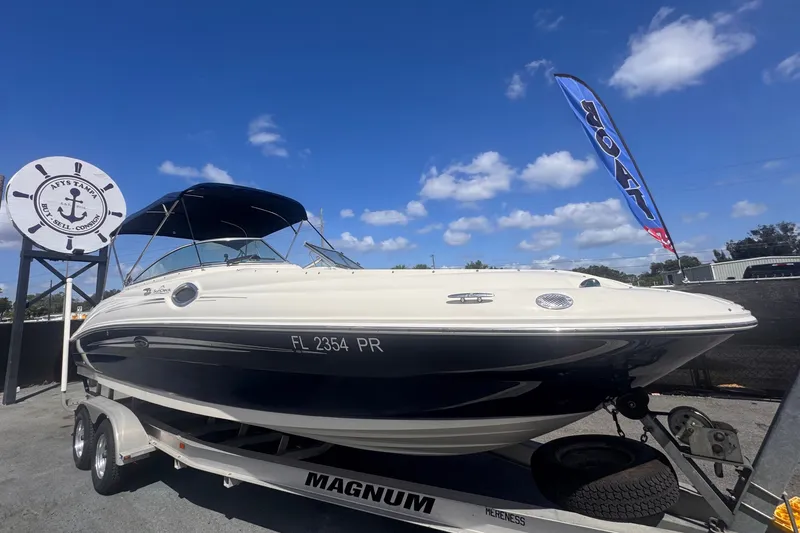 The Image of A 2008 Sea Ray 240 Sundeck on a trailer, featuring a blue canopy and a flag in the background. - 0