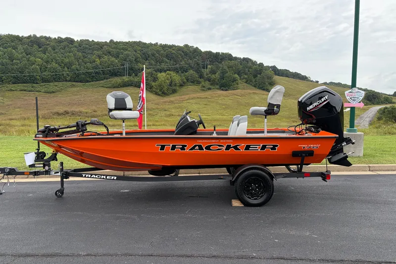 The Image of 2027 Tracker Pro Team 175 boat, bright orange, parked on a trailer, scenic background. - 0