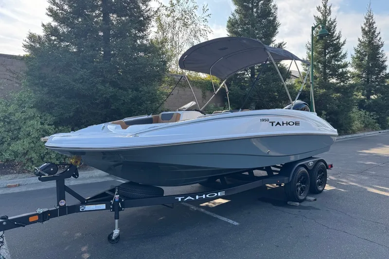 Slide: The Image of 2027 Tahoe 1950 boat on trailer, parked outdoors with trees in background. - 2