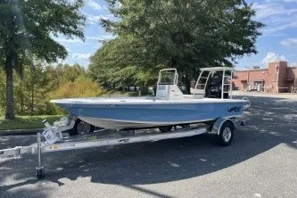 Slide: The Image of 2026 Mako 18 Pro Skiff boat on trailer, parked outdoors near trees and building. - 1