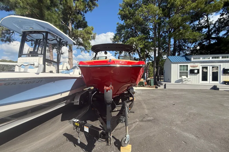 Slide: The Image of 2024 MasterCraft XT22 boat in vibrant red, parked outdoors beside another boat. - 15