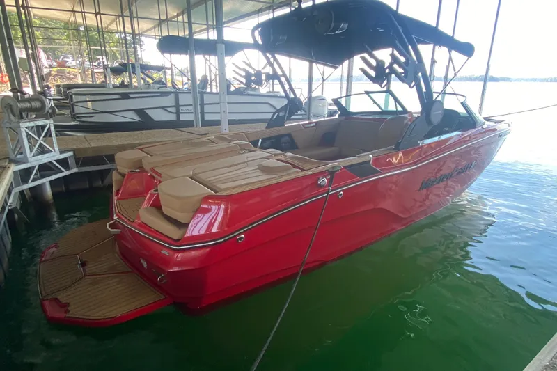 Slide: The Image of 2024 MasterCraft XT22 boat in vibrant red, docked on calm water. - 2