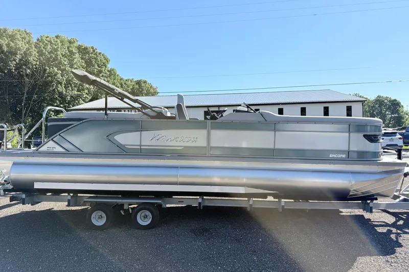 The Image of 2027 Manitou Encore 25 RFSHP575 pontoon boat on trailer, parked outdoors. - 0