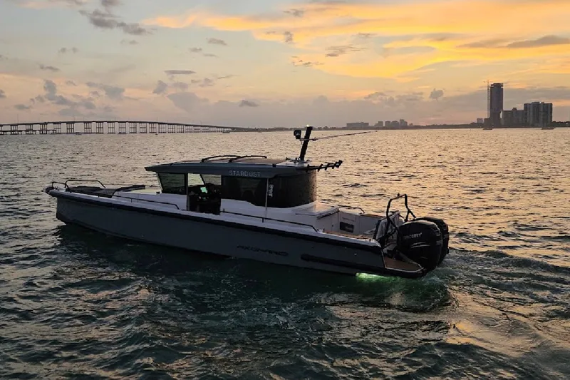 The Image of 2021 Axopar 37 XC Cross Cabin boat cruising at sunset near a city skyline. - 1