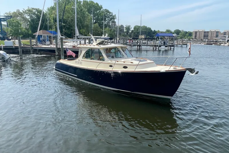 Slide: The Image of 2014 Hinckley Talaria 34 yacht docked in a marina, surrounded by calm waters and sailboats. - 2