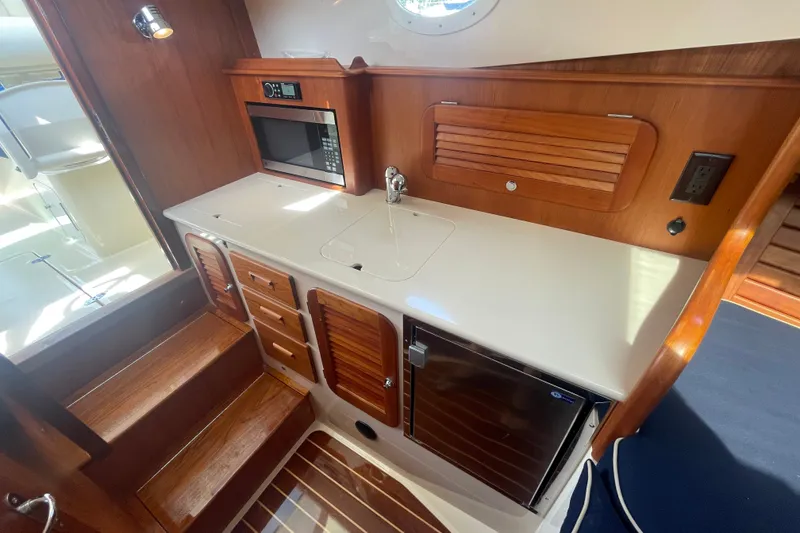 Slide: The Image of Hinckley Talaria 34 yacht interior, featuring a compact kitchen with wood cabinetry and modern appliances. - 14