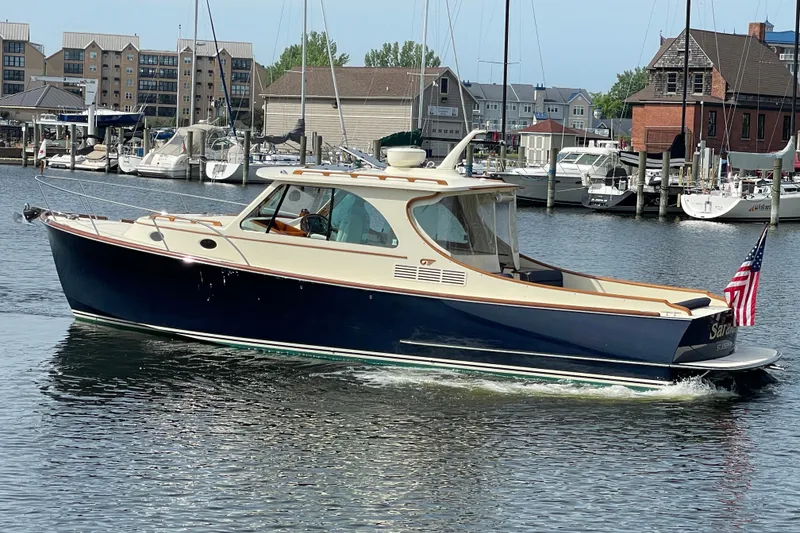 The Image of 2014 Hinckley Talaria 34 yacht cruising in a marina with docked boats in the background. - 0