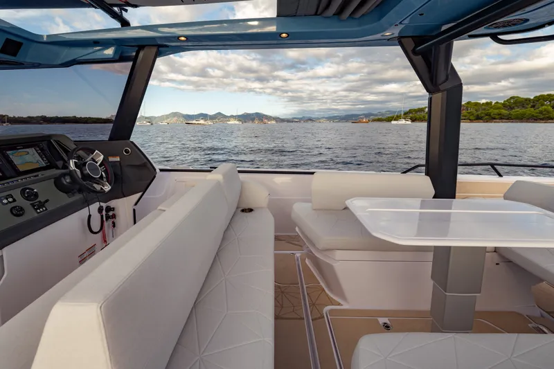 Slide: The Image of Interior view of 2027 Axopar 38 Cross Top boat with seating and table, overlooking scenic water. - 26