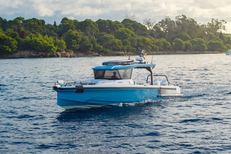 The Image of Axopar 38 Cross Top 2027 on calm water near a wooded coastline. - 0