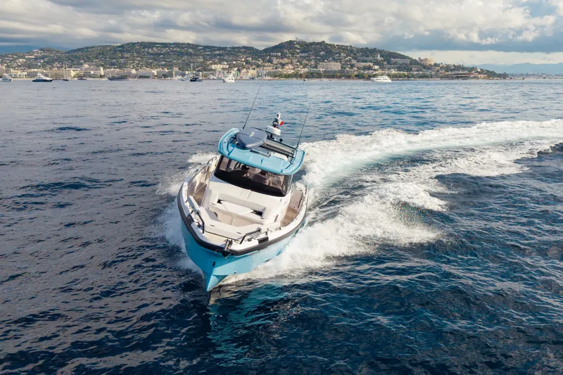 Slide: The Image of 2027 Axopar 38 Cross Top cruising on open water near a coastal city. - 5