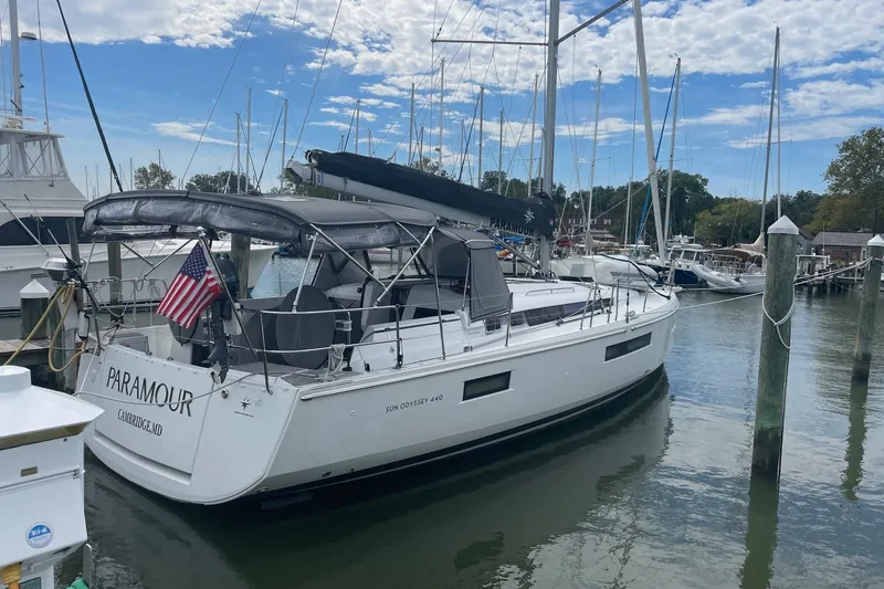 The Image of 2022 Jeanneau Sun Odyssey 440 sailboat docked in a marina under a partly cloudy sky. - 0