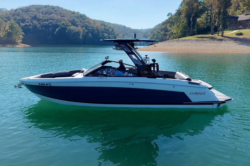 Slide: The Image of 2022 Cobalt R8 Surf boat on a serene lake with lush green surroundings. - 18