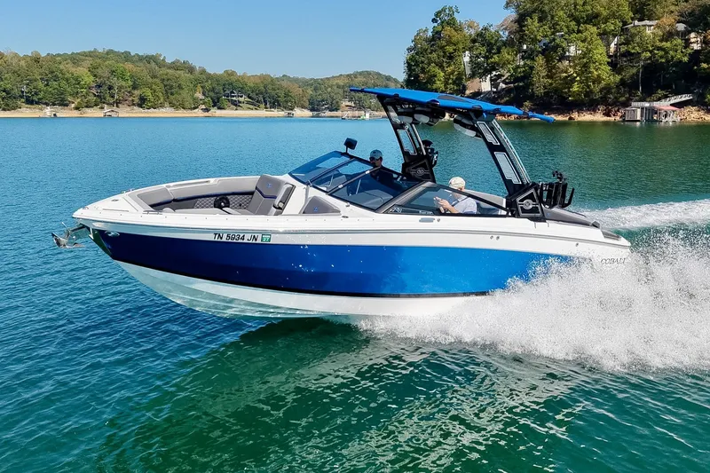 The Image of 2022 Cobalt R8 Surf boat cruising on a scenic lake with lush green surroundings. - 0