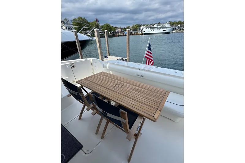 Slide: The Image of 2005 Sea Ray 550 Sedan Bridge yacht deck with wooden table and chairs, docked by the water. - 32