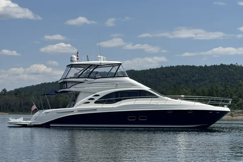Slide: The Image of 2005 Sea Ray 550 Sedan Bridge yacht on calm water with scenic forest backdrop. - 1