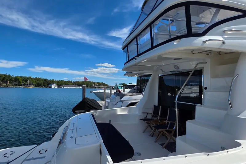 Slide: The Image of 2005 Sea Ray 550 Sedan Bridge yacht docked by a serene lake under a clear blue sky. - 58